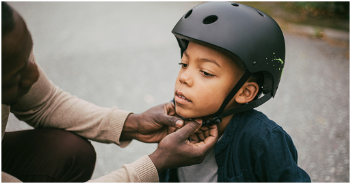 A parent buckles up the helmet of his child