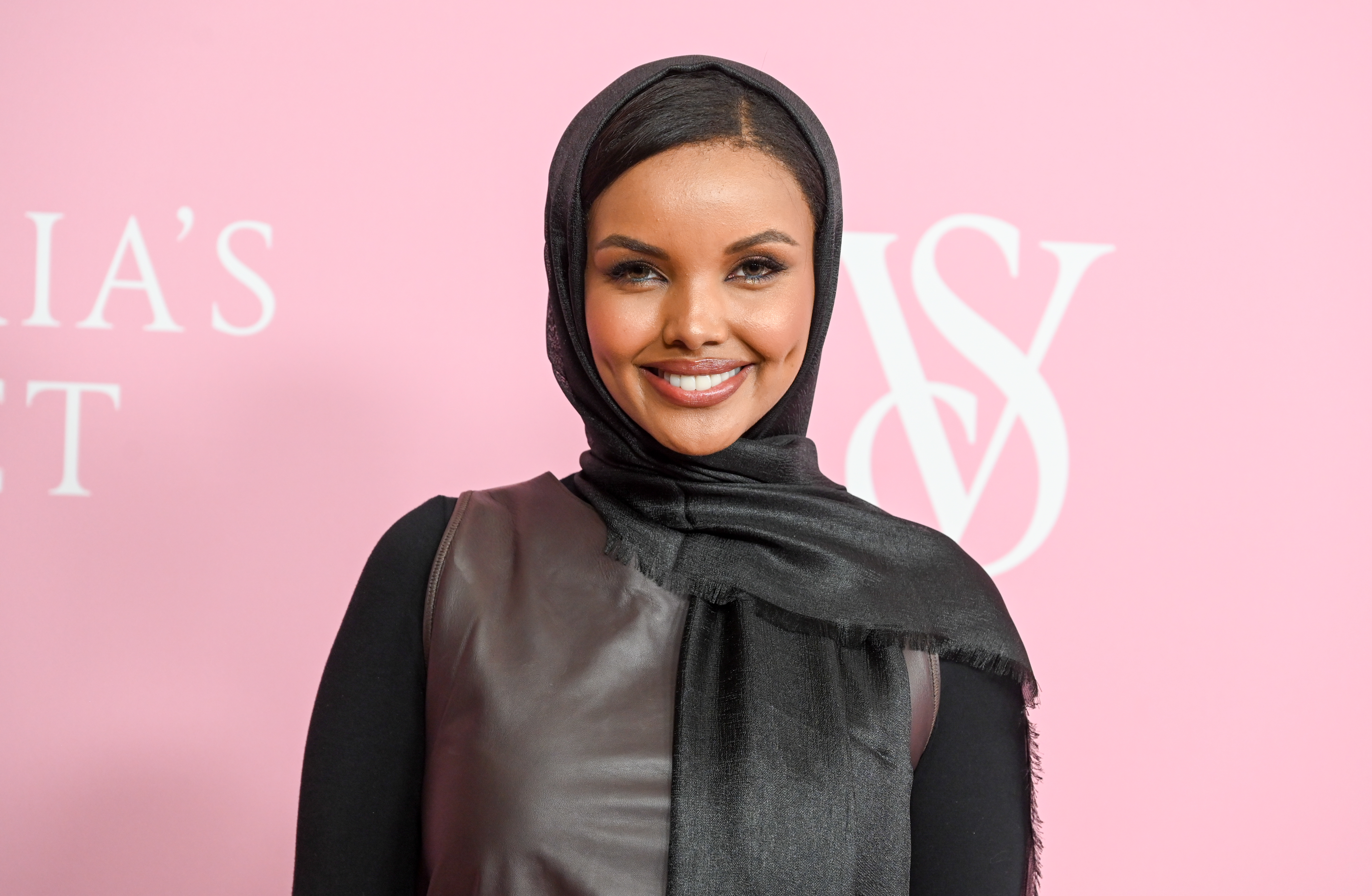 Halima Aden, in a black and brown outfit, smiles for a photo in New York, New York