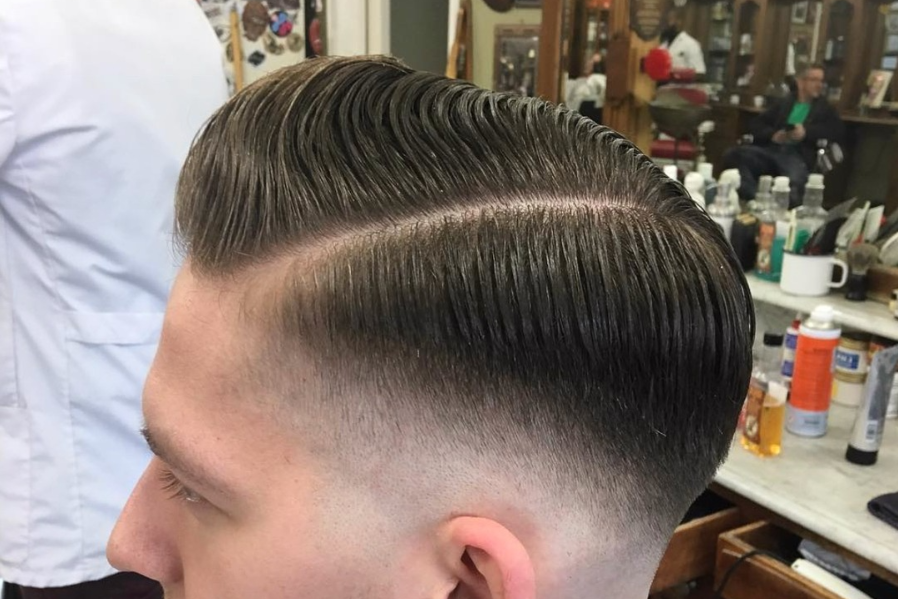 A man with a pompadour haircut is inside a barber shop