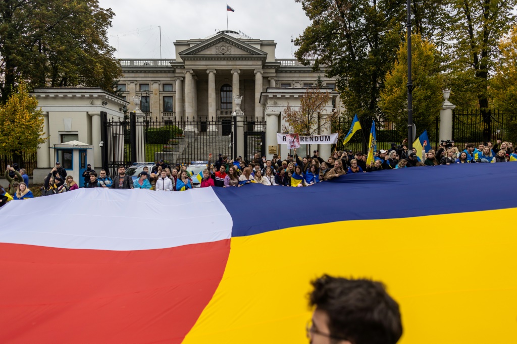 People hold a giant banner made of Poland and Ukraine's flags while attending a mock referendum on whether Warsaw should annex Russia's embassy