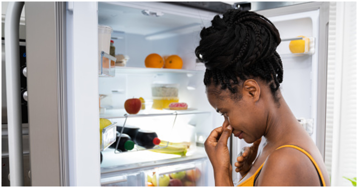 A lady holds her nose because of a bad smell from her fridge