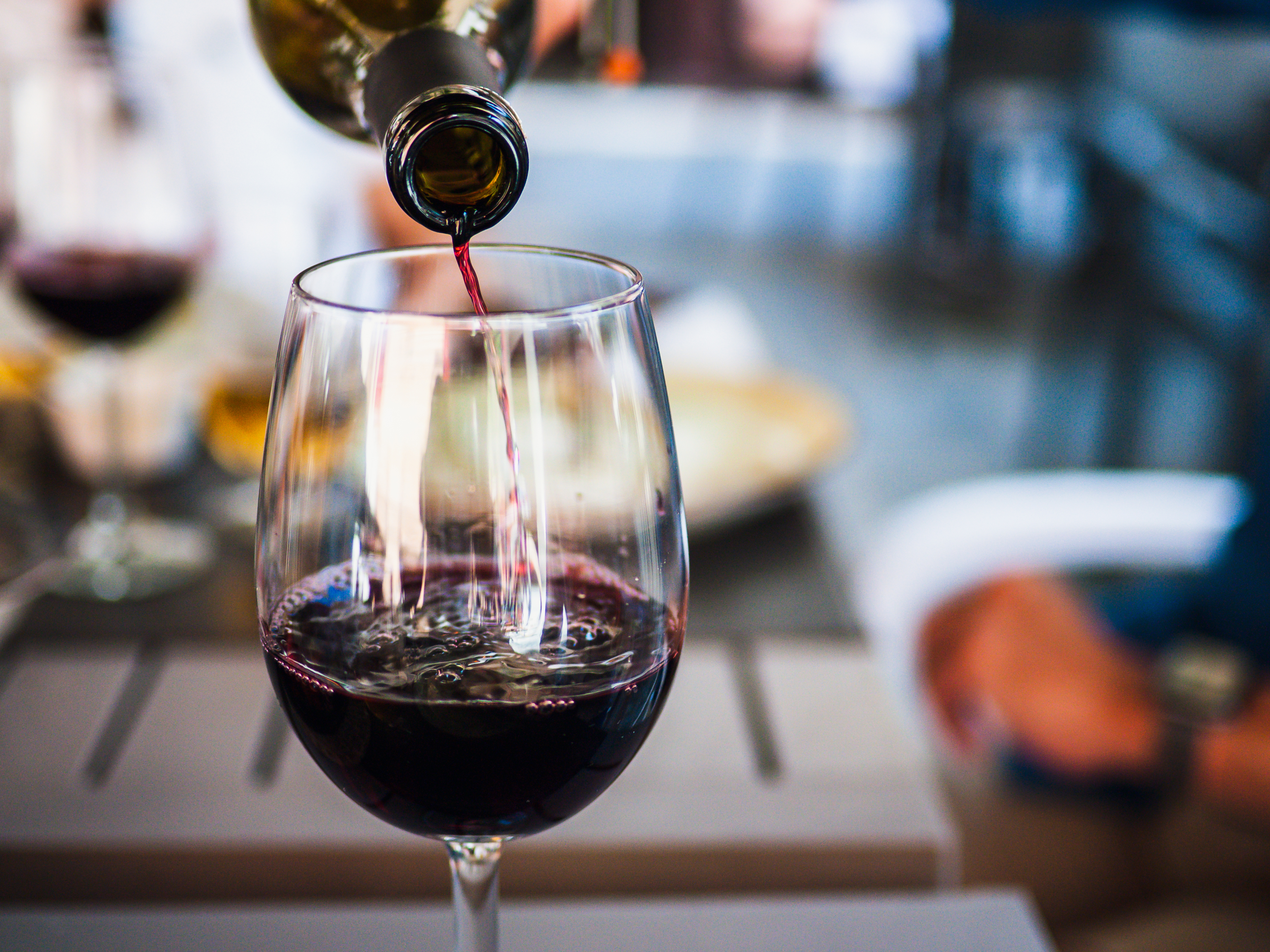 An image of someone pouring red wine in a Bordeaux wine glass.