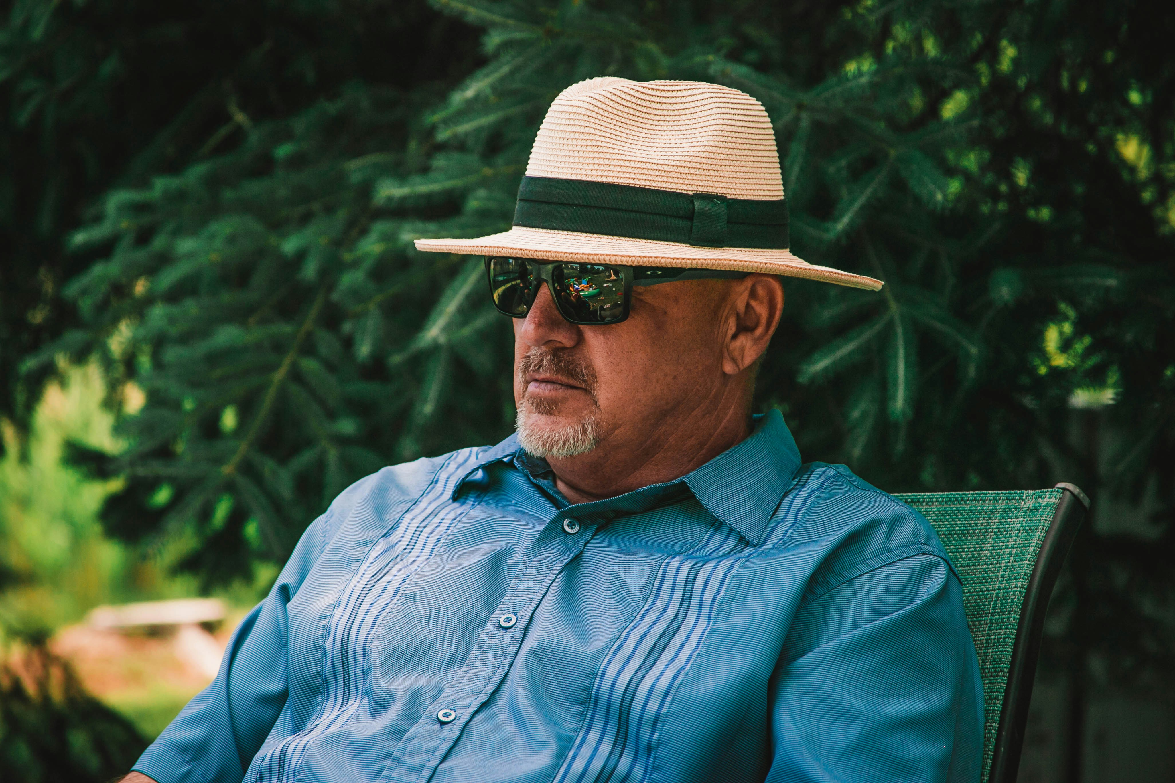 A man is dressed in a blue shirt, sunglasses, and a Panama hat