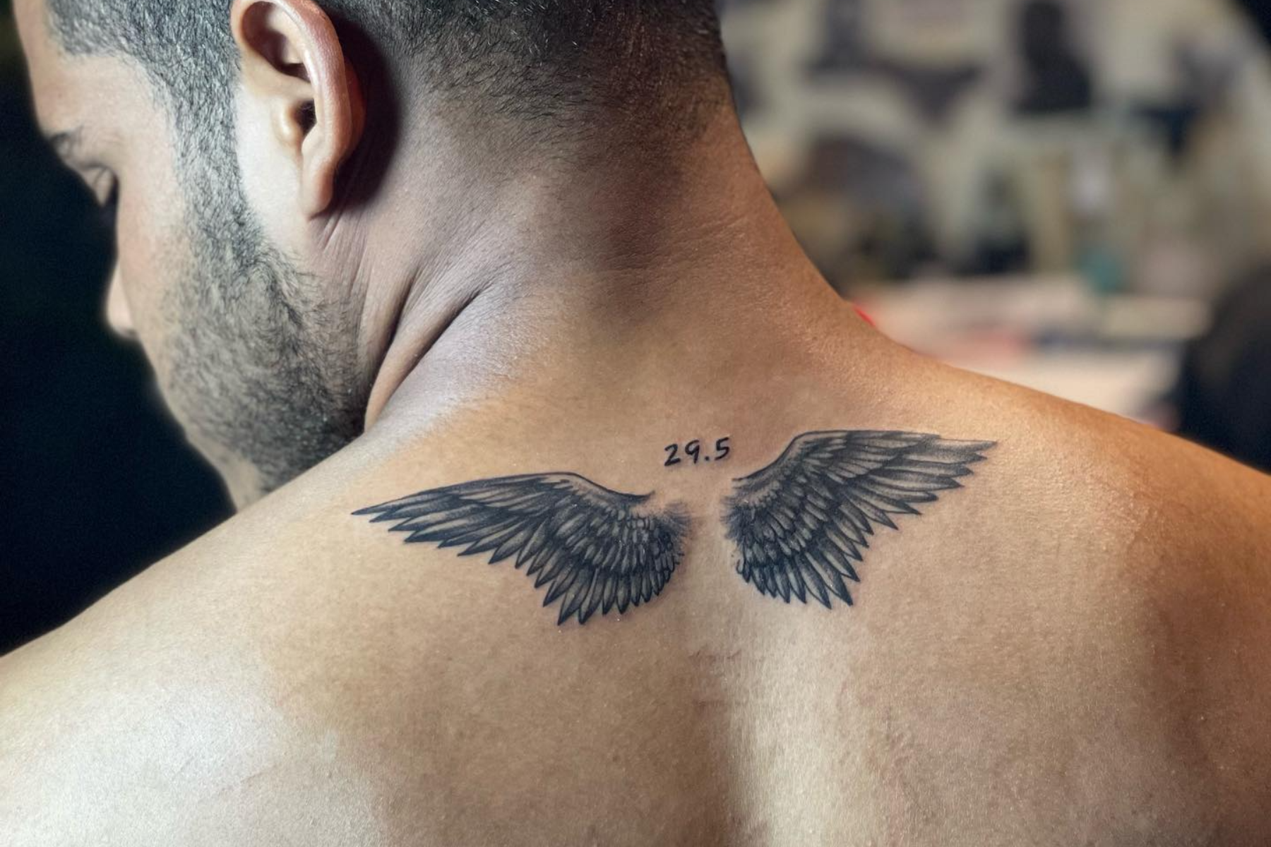A man is donning a small wing tattoo on his upper back
