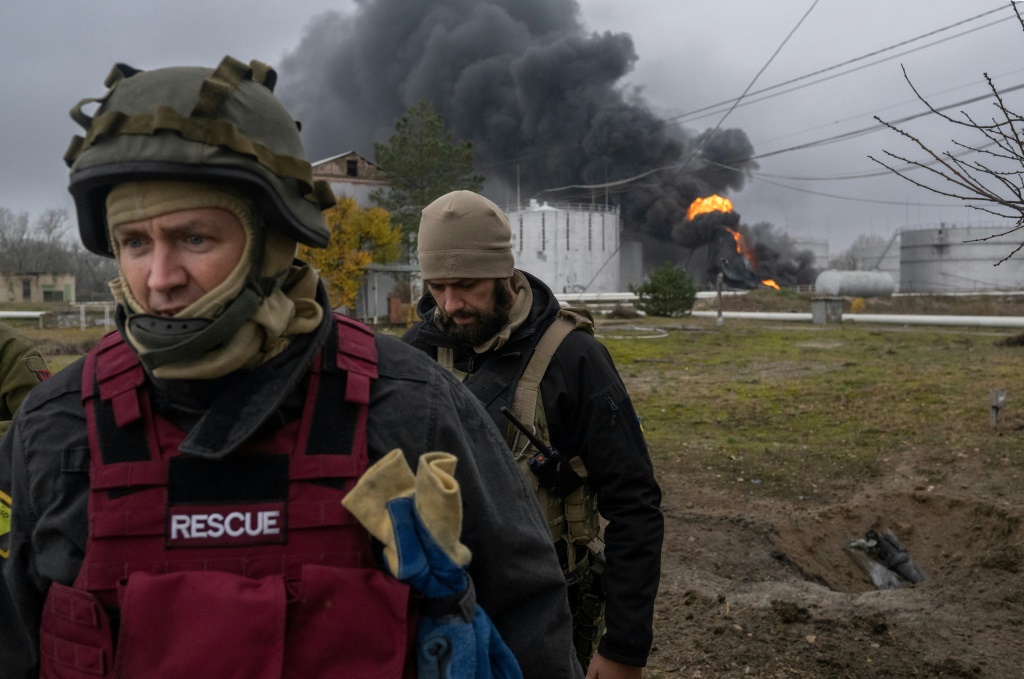 A Ukrainian rescue service member and a soldier inspect the area as black smoke rises from an oil reserve in Kherson