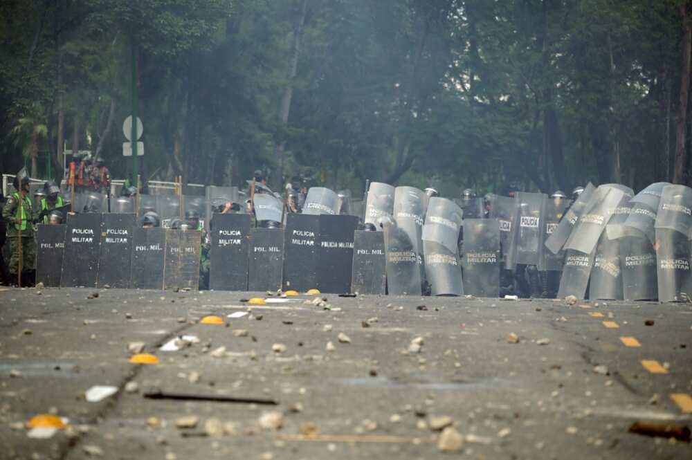 Mexican military police take cover from stones and homemade explosive devices thrown during a demonstration at an army camp over the disappearance of 43 students in 2014