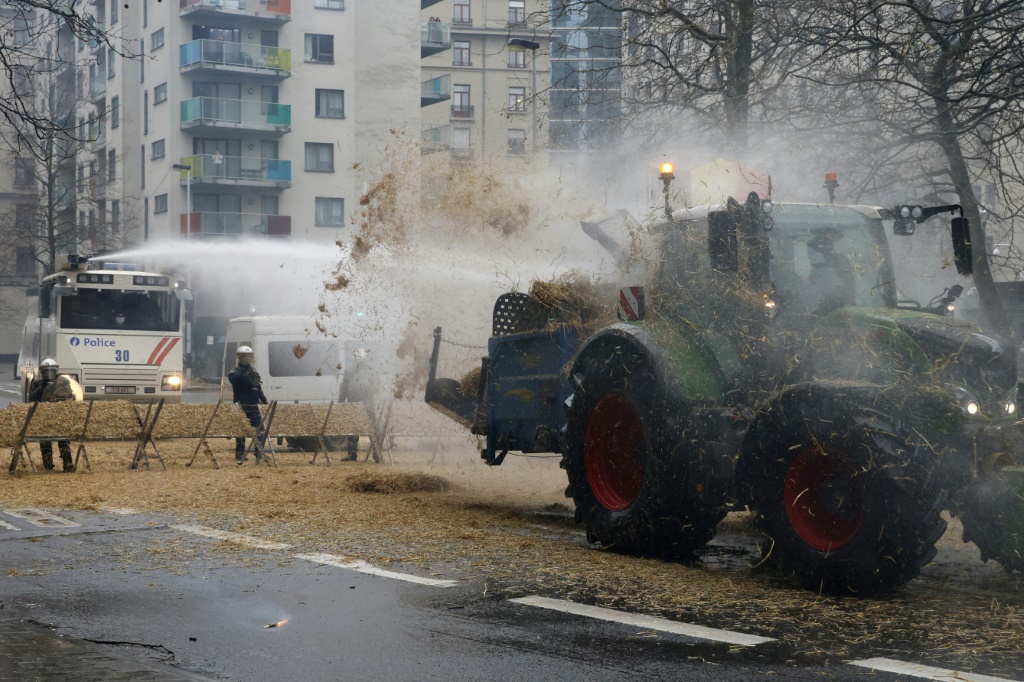 A tractor discharges hay onto riot police officers in Brussels, on February 26, 2024