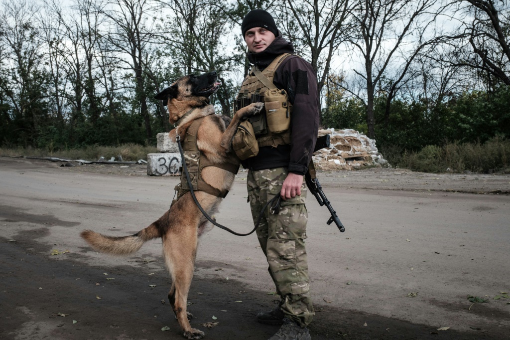 National Police officer Andriy Symchuk stands with his sniffer dog 'Bars' at a checkpoint in Izyum, a Ukrainian city where a mass grave was found after Russian invaders were driven out