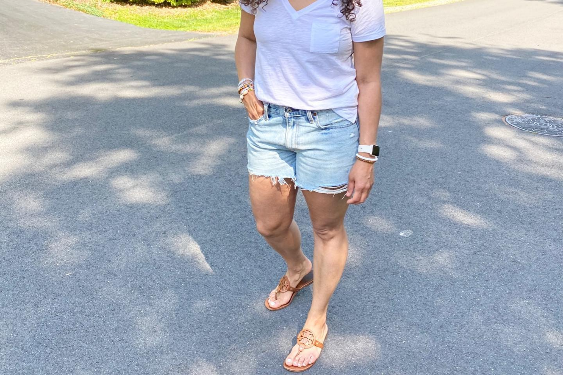 A lady is wearing a denim cutoff with a white t-shirt.