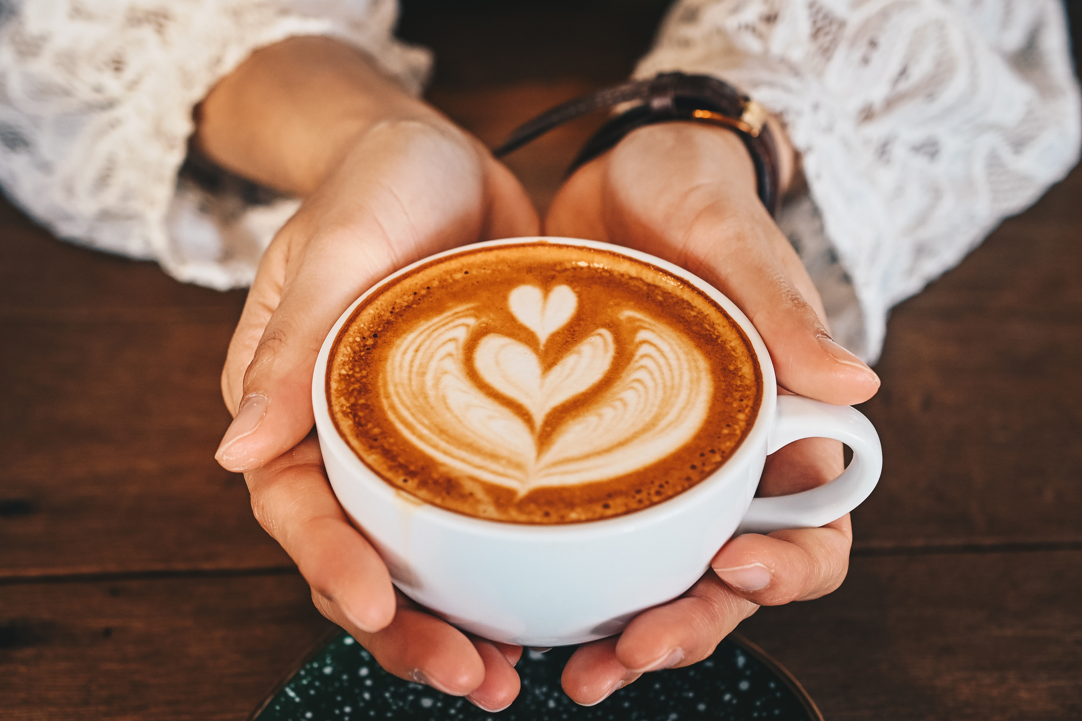 A cropped shot of a woman's hands holding a cup of hot latte coffee