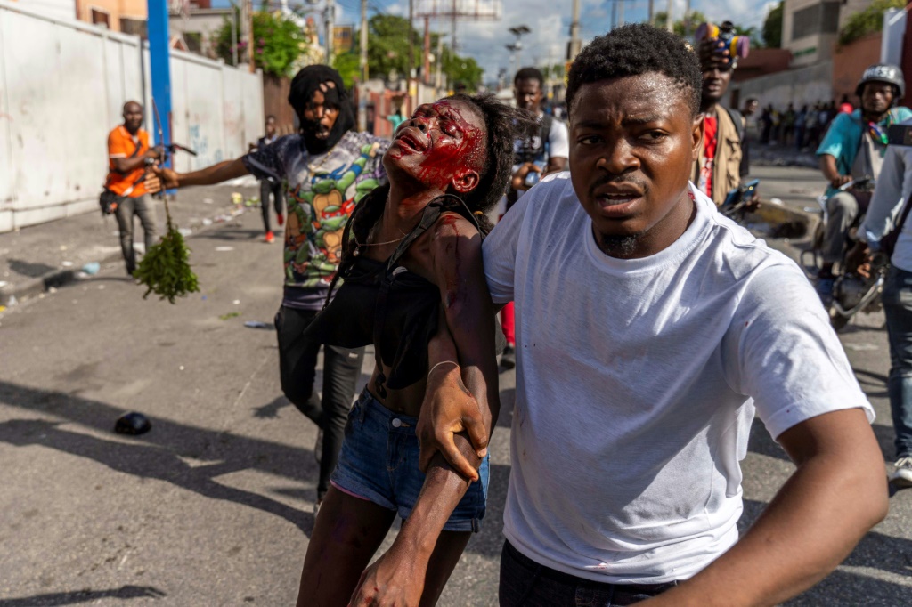 A man assists an injured woman during a protest against Haitian Prime Minister Ariel Henry calling for his resignation, in Port-au-Prince, October 10, 2022
