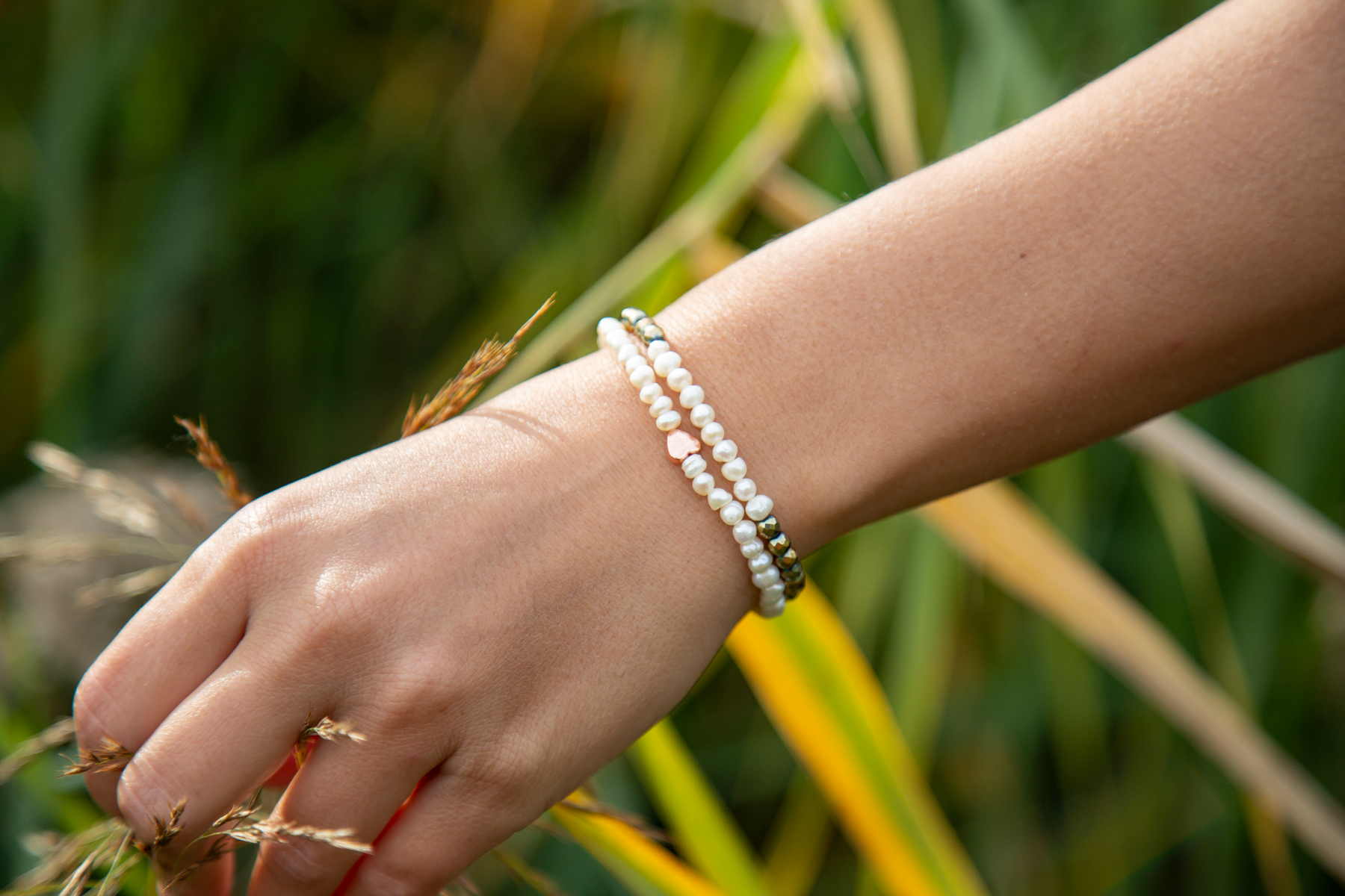 A hand shows off a pair of white and gold pearl bracelets