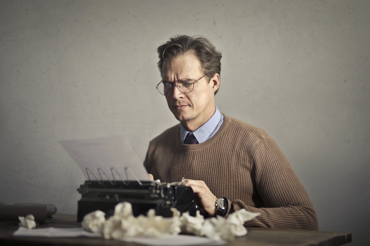 An adult frowned male writer working on a typewriter at home