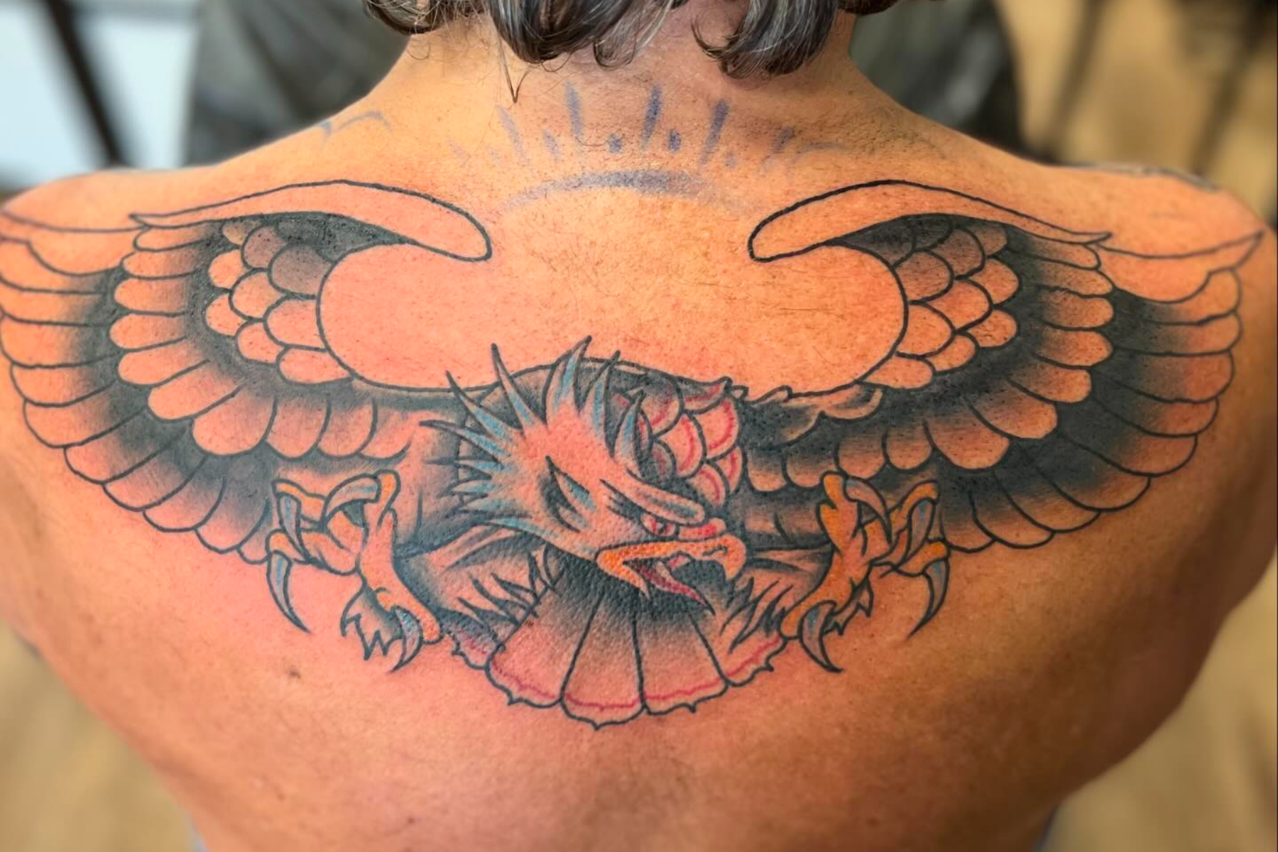 A man is having an eagle tattoo on his upper back