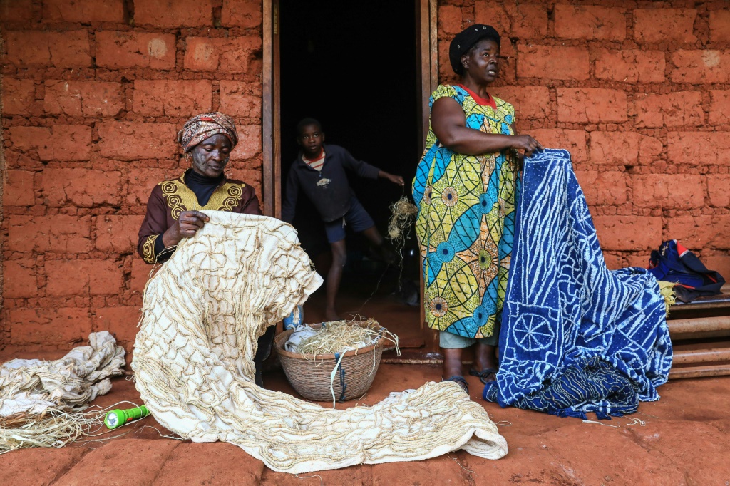 Yougo's cousin Sylvie Momo (right) holds up a dyed ndop outside her home in Baham