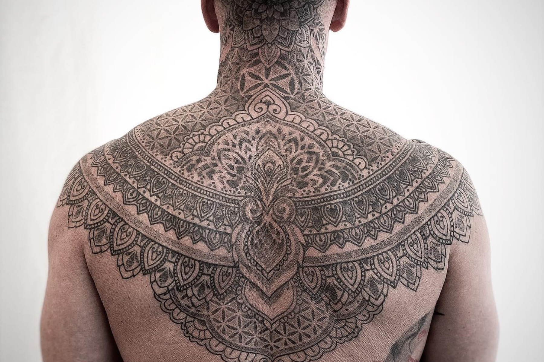 A man has a mandala tattoo across his shoulders and back