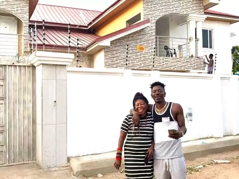Shatta Wale and his mother standing in front of a house