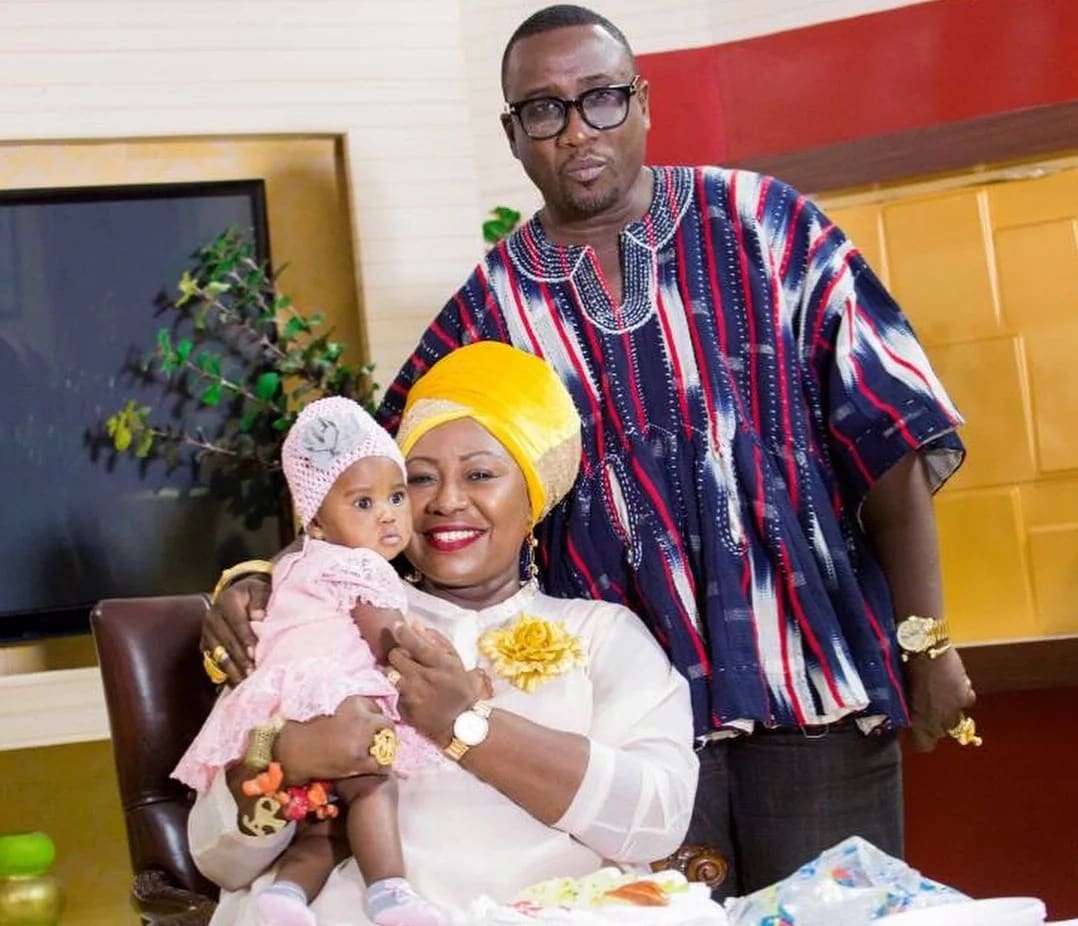 Gifty Anti sits with her baby as her husband stands behind her