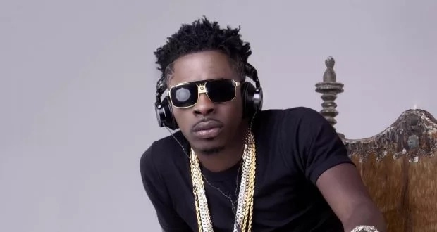 Shatta Wale sitting down with large gold chains around his neck