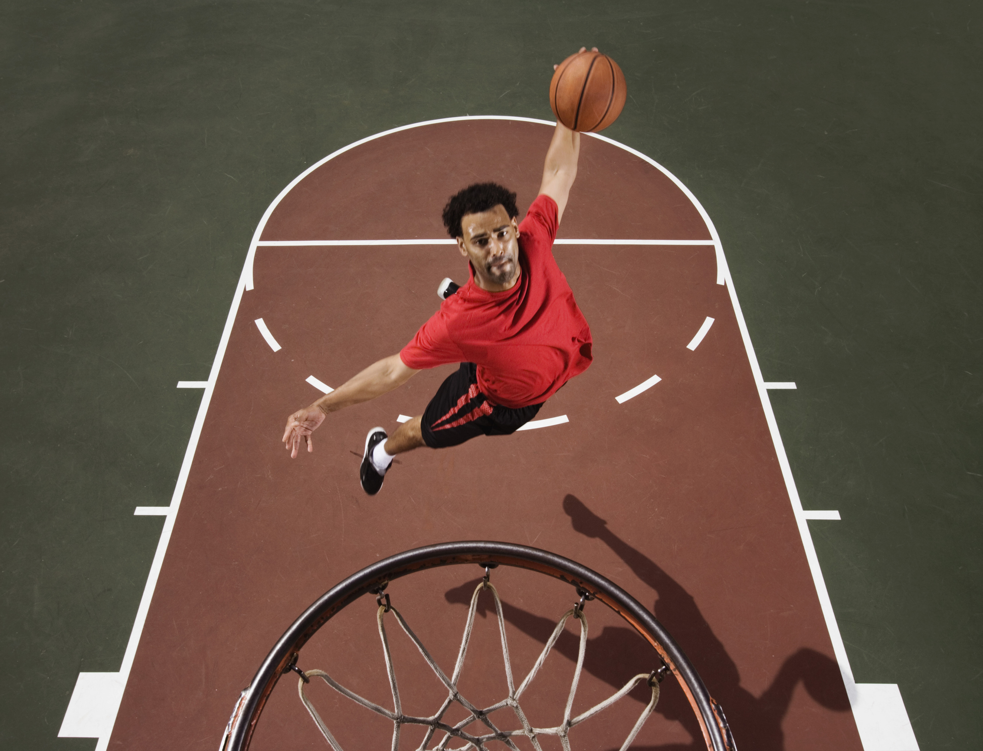 An individual in red attire jumping up to slam dunk a basketball.