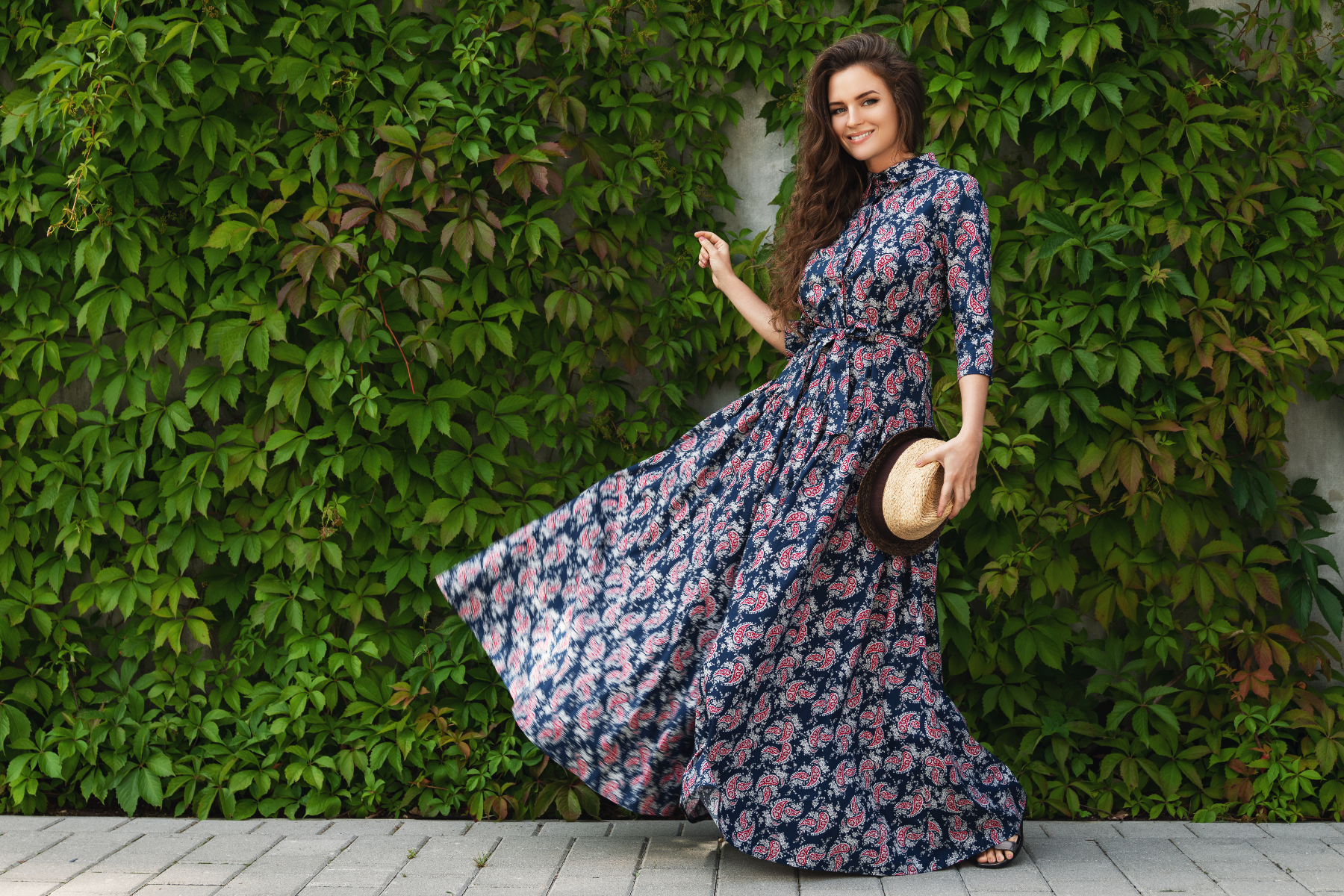 A gorgeous woman wearing a beautiful maxi dress poses against the wall with a wild grape
