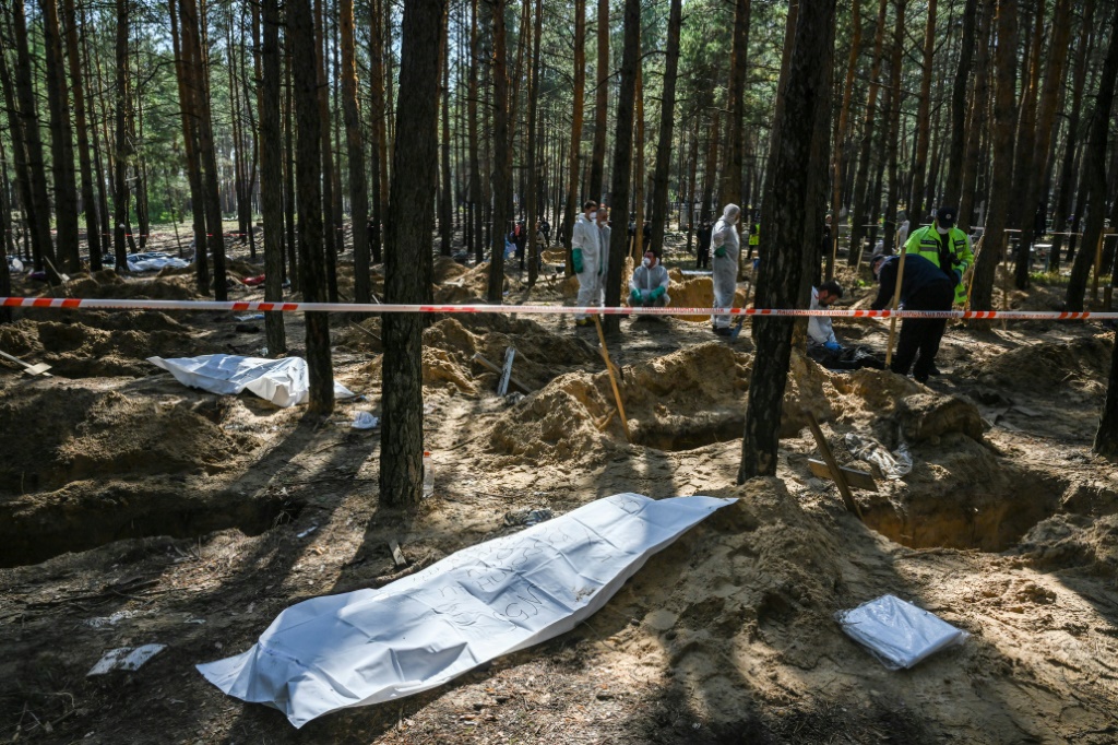 Forensic technicians exhume bodies and place them in body bags at a mass grave site on the outskirts of Izyum