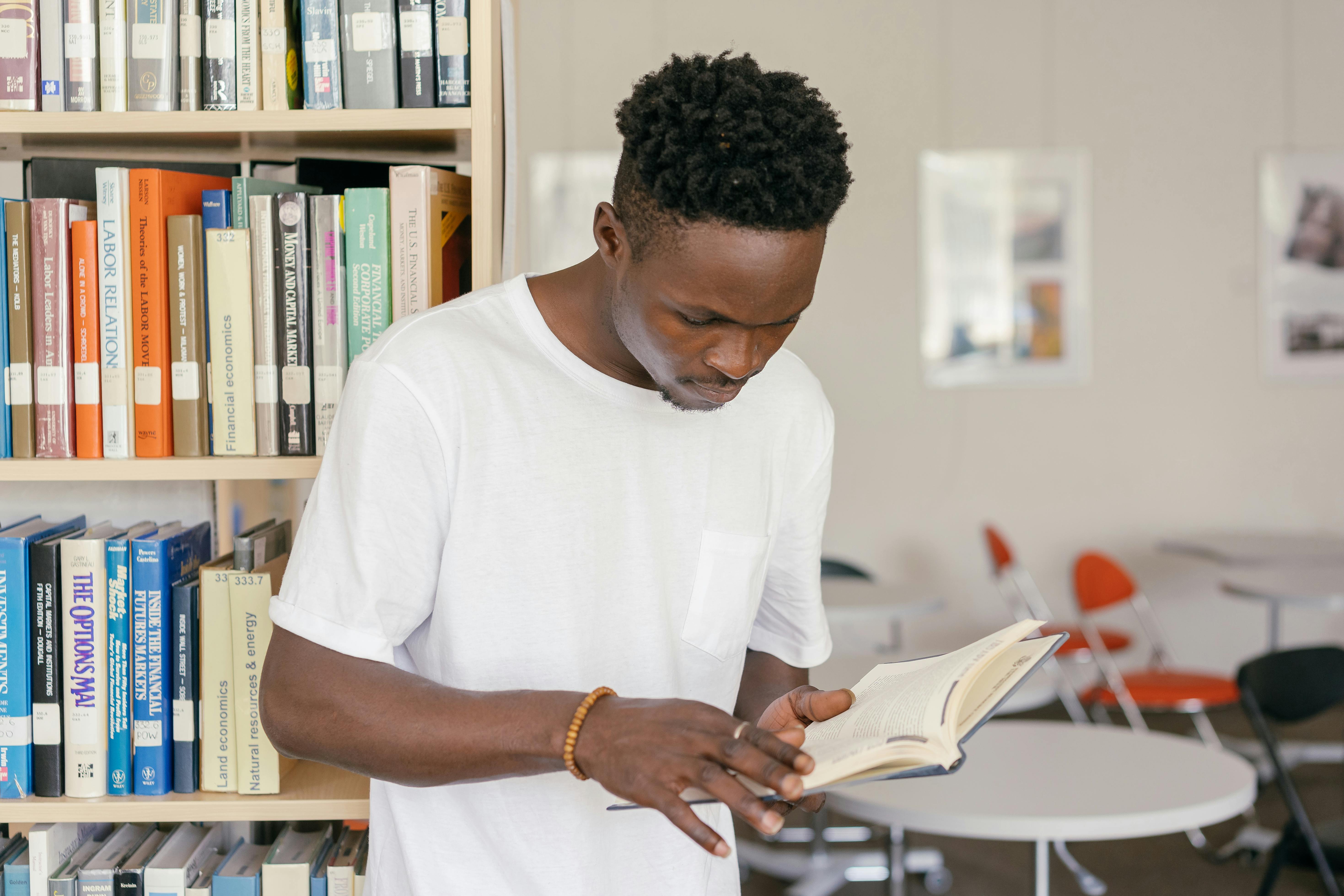 A man in a white shirt is reading a book in a library