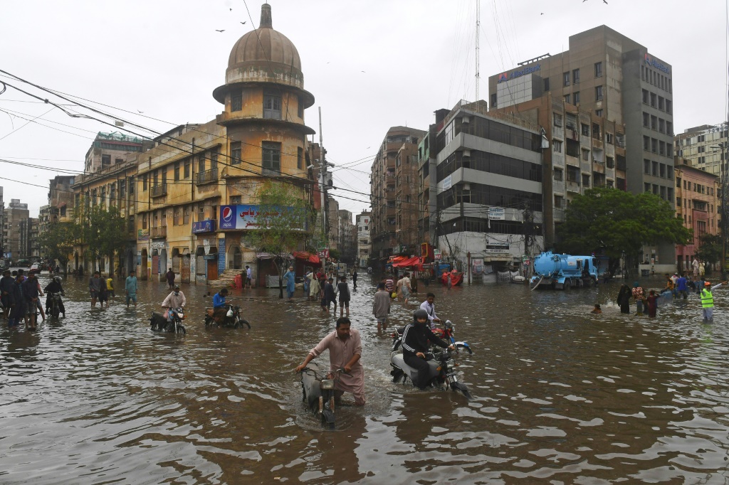 Motorcyclists push their vehicles through a flooded street in Pakistan's port city of Karachi