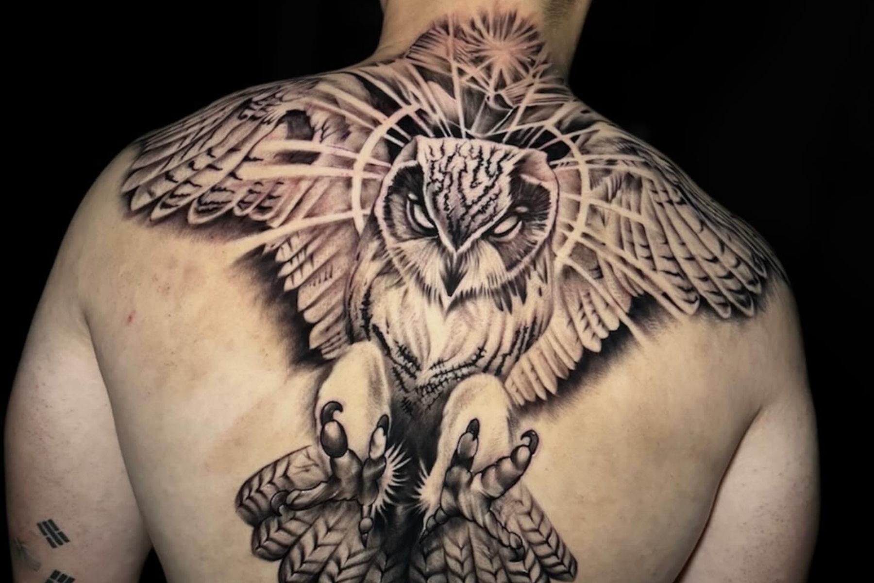 A man has an owl tattoo on his upper and middle back
