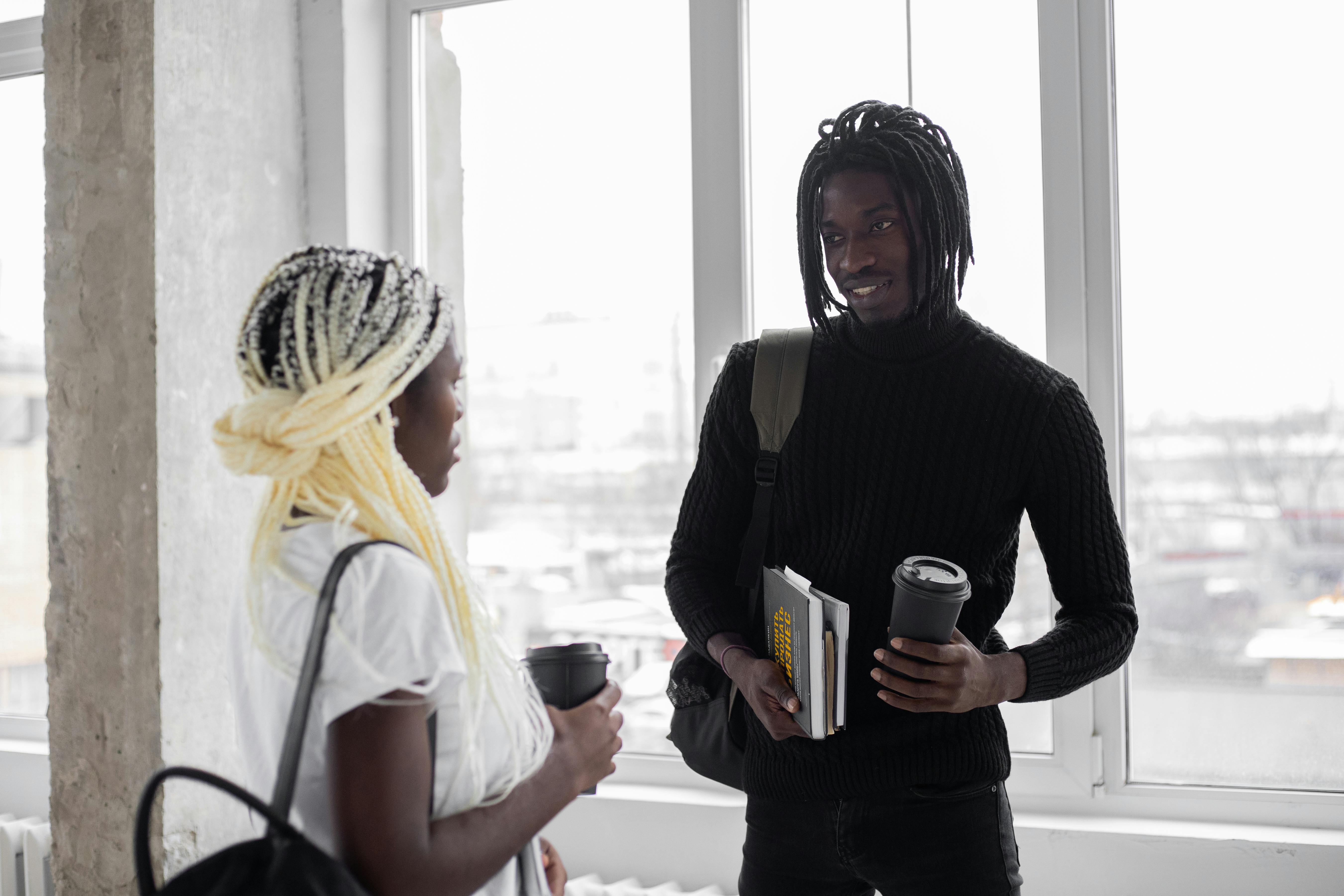 A male and female student talking as they have takeaway coffee