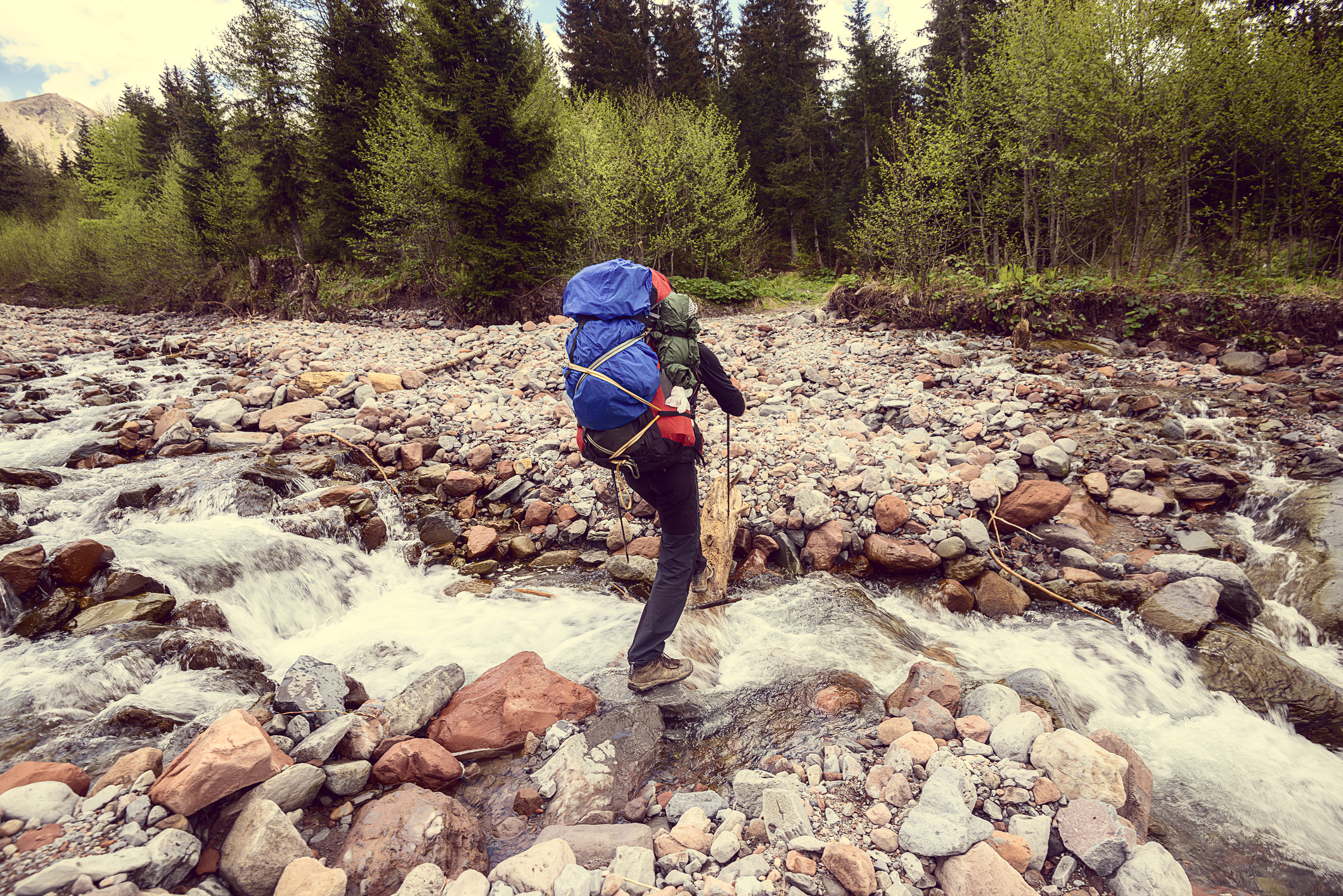 A traveller with a backpack crosses a mountain river.