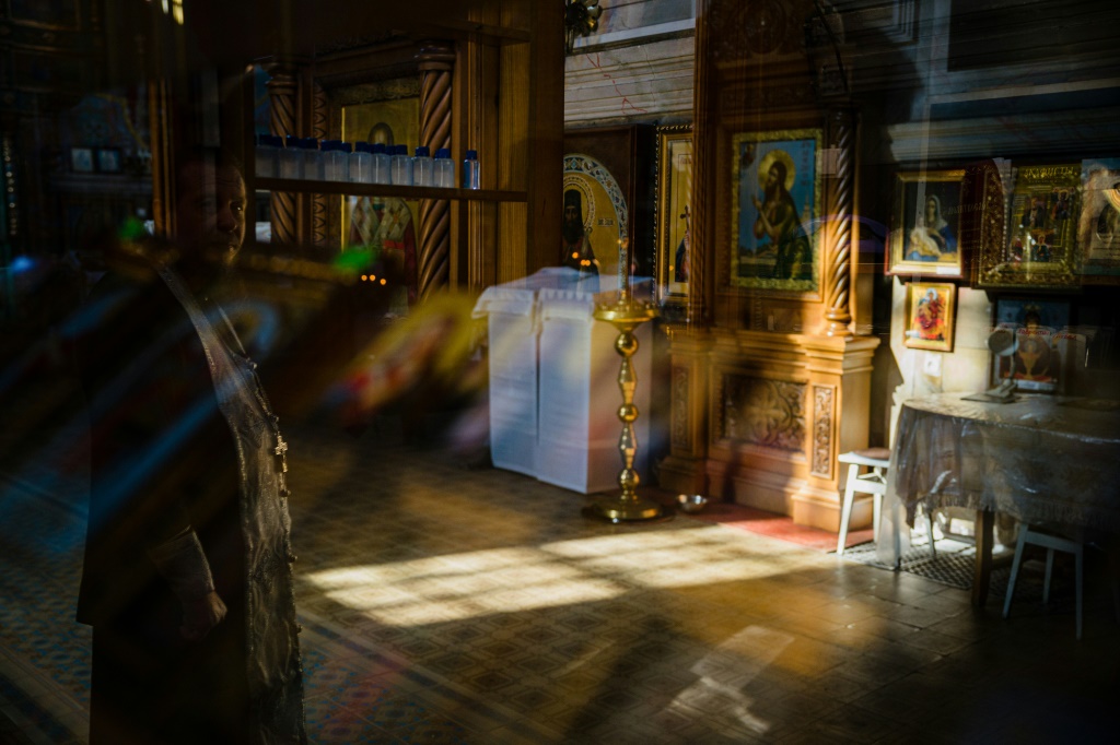 Orthodox priest Semyon reflected in a window in a church Izyum after its recapture