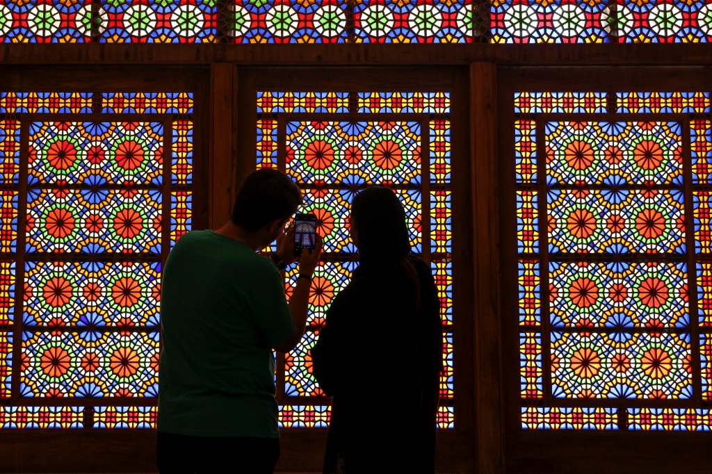 A man and a woman stand in front a stained glass window at Dowlat Abad Garden in Iran's central city of Yazd on July 3, 2023