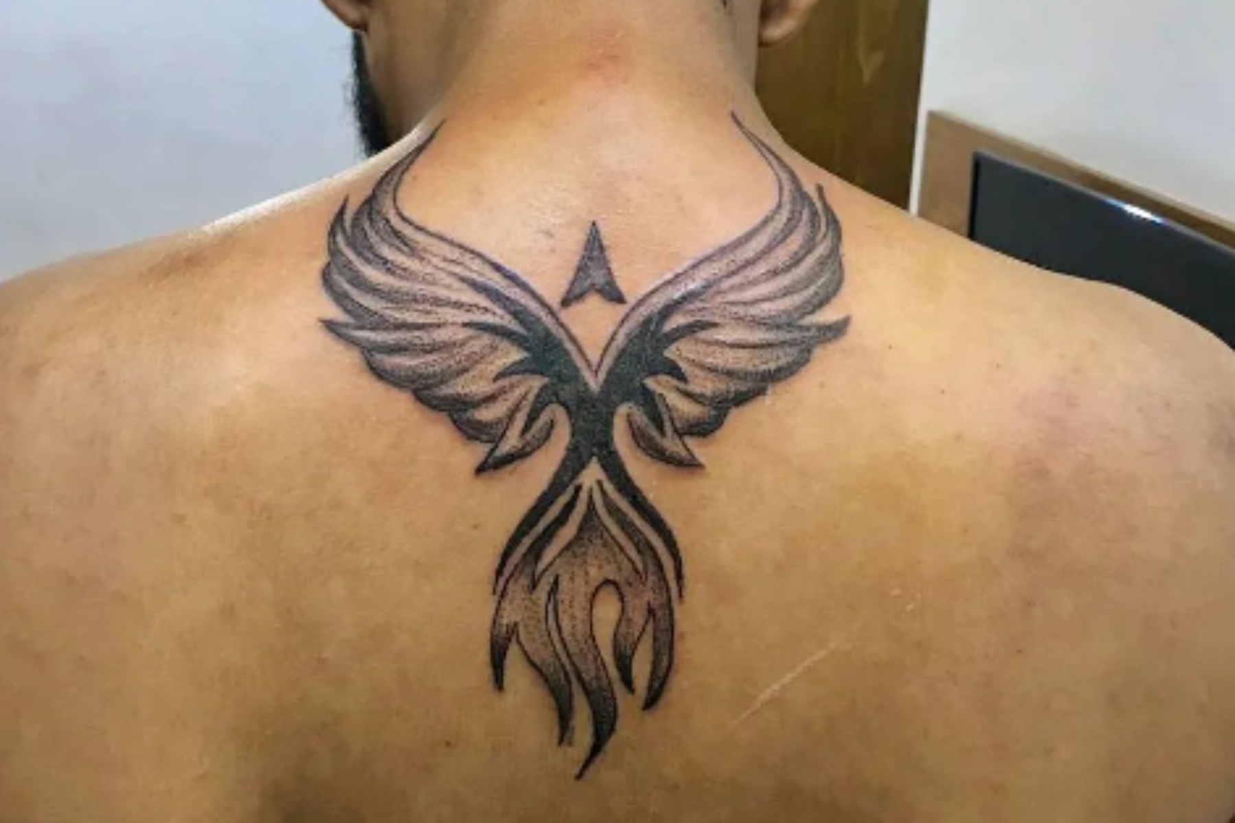 A man has a phoenix tattoo on his upper middle part