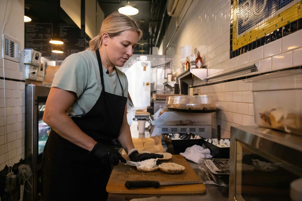 Ashley Dikos, wife of Bo's Bagels owner Andrew Martinez, spreads cream cheese on bagels at their restaurant in Harlem