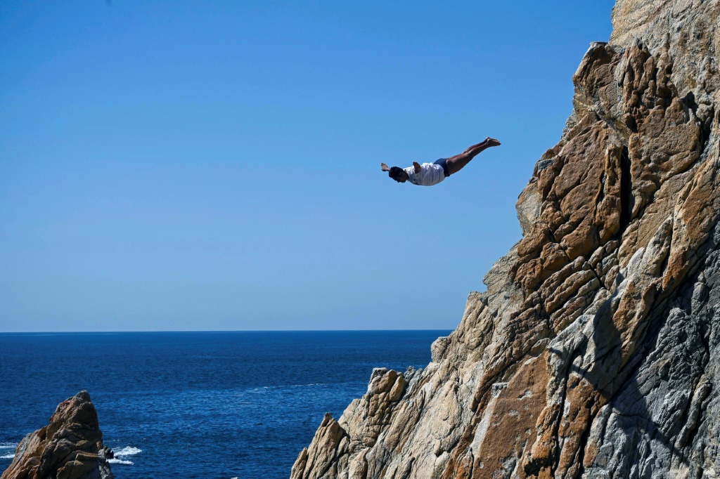 A cliff diver leaps from the rocks above Acapulco after the Mexican resort allowed resumption of the  activity in the aftermath of deadly Hurricane Otis, but tourists are only slowly returning to the region