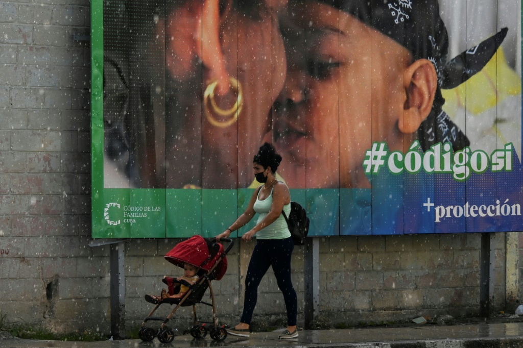 A woman and her baby walk past a banner in Havana promoting a mew family code that legalizes same-sex marriage and other rights