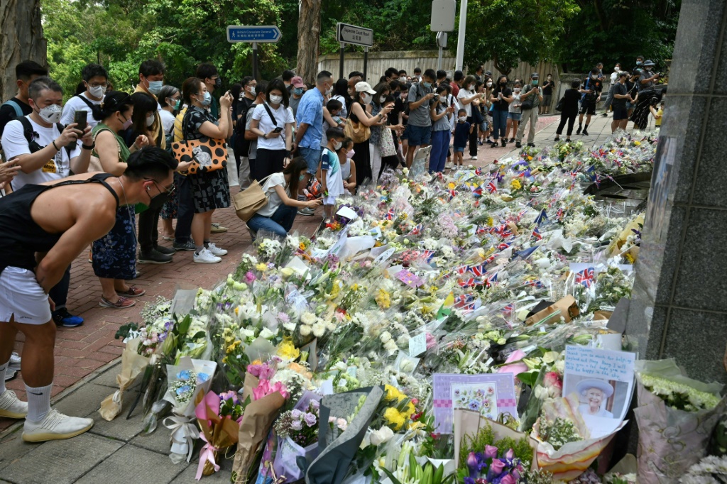 People gather next to flowers placed as a tribute to Queen Elizabeth outside the British consulate in Hong Kong