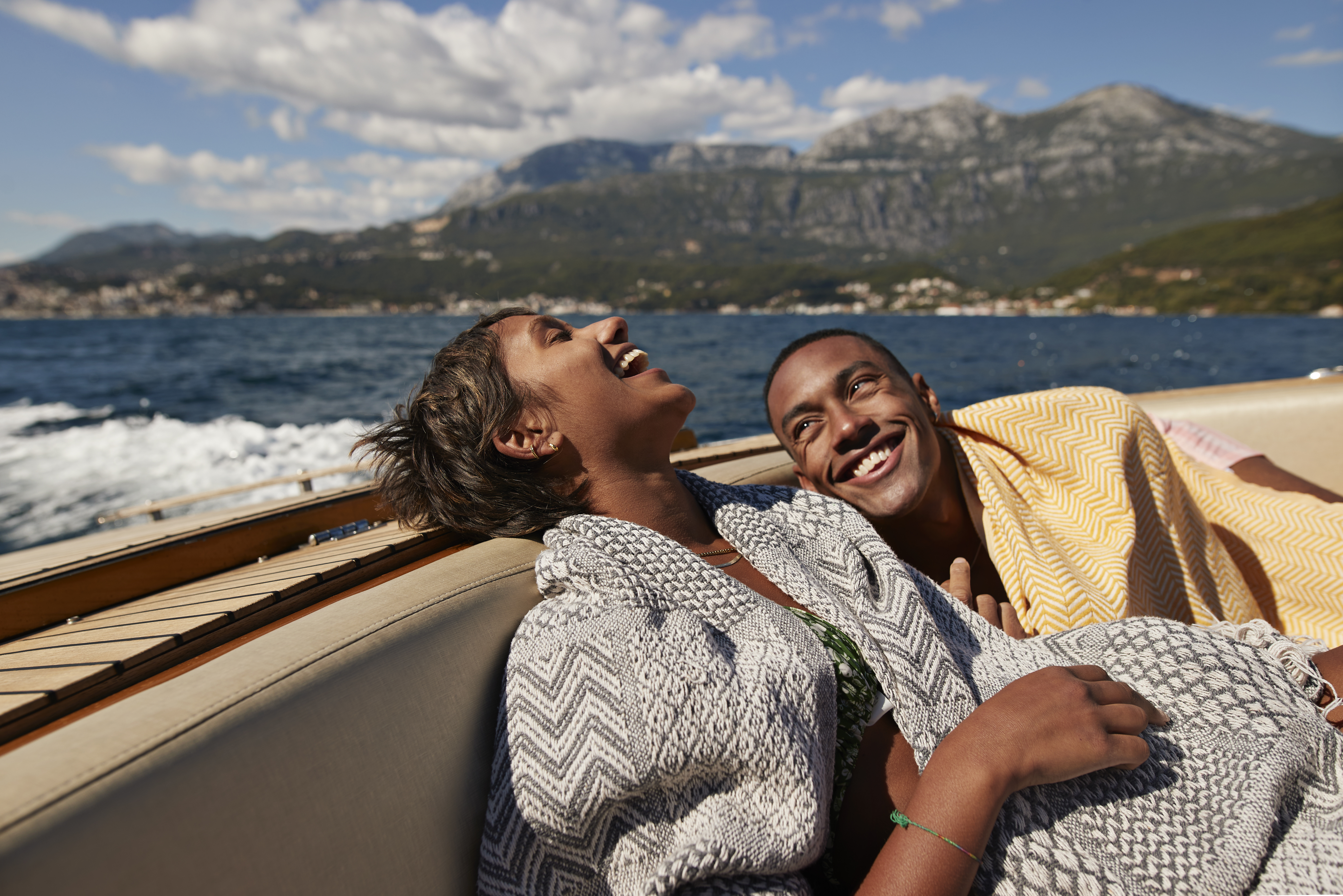 Young man and woman laughing in speedboat enjoying summer on sunny day