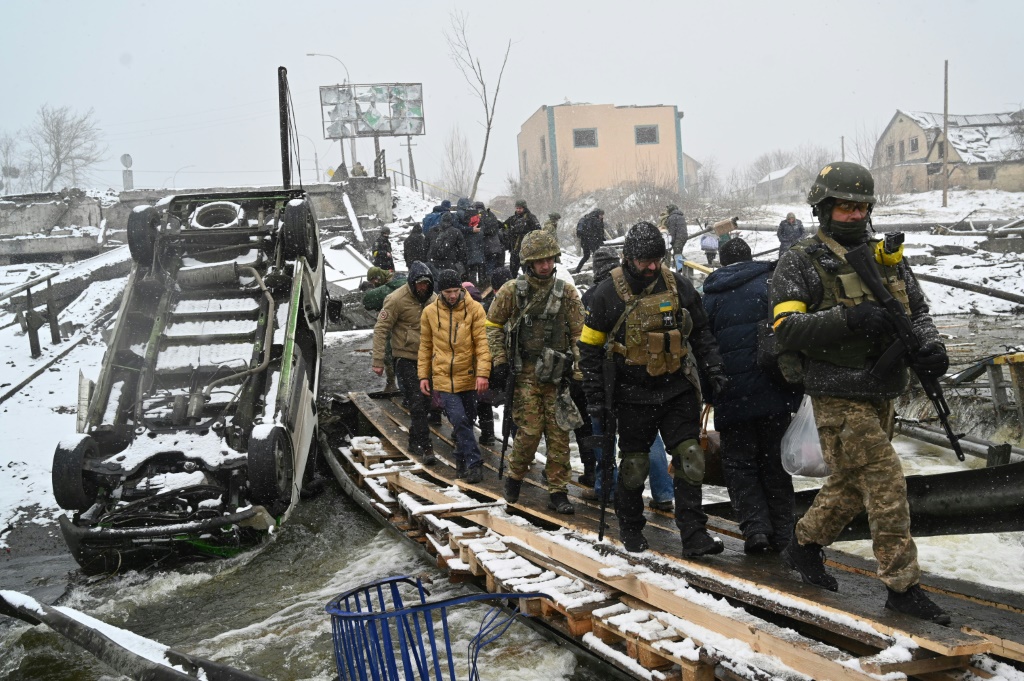 Ukrainian soldiers walk across a destroyed bridge northwest of Kyiv in March 2022