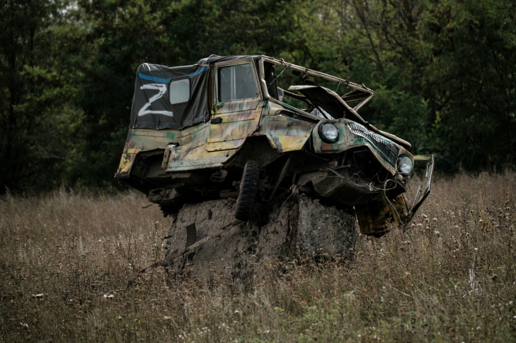 A damaged car bearing the letter 'Z', the symbol of Russian forces, sits at a possible mine field near a suspected mass grave in Kozacha Lopan