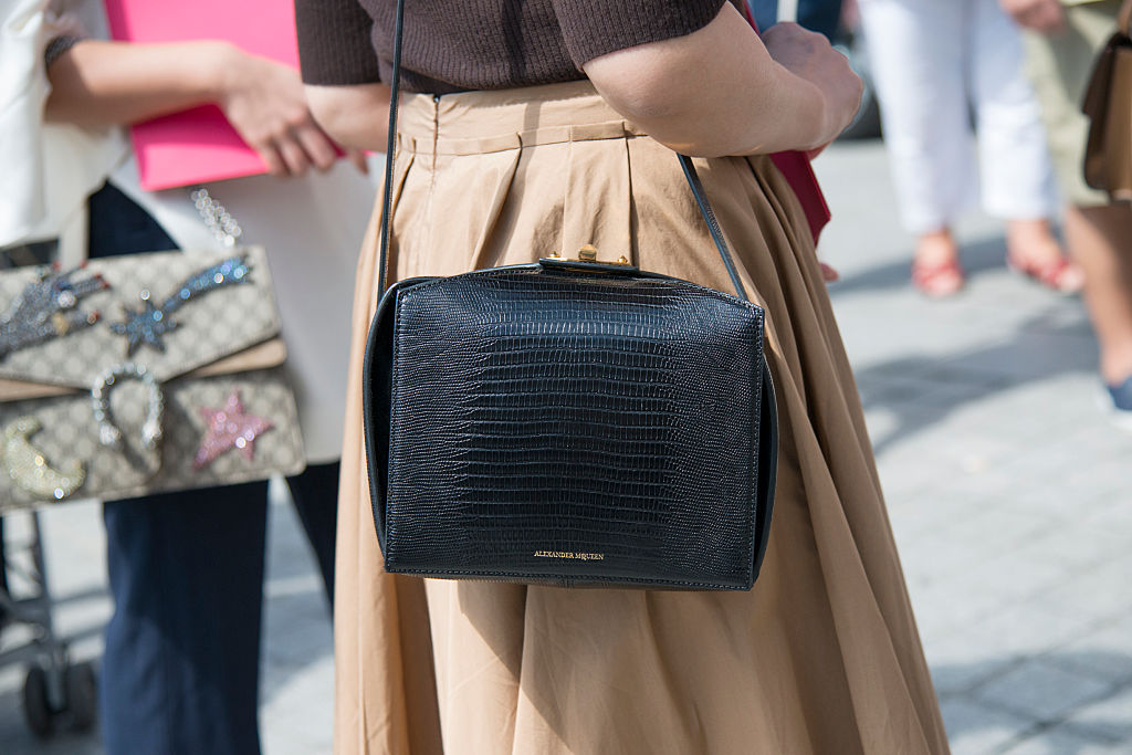 A woman stylishly carries an Alexander McQueen black purse on her shoulder.