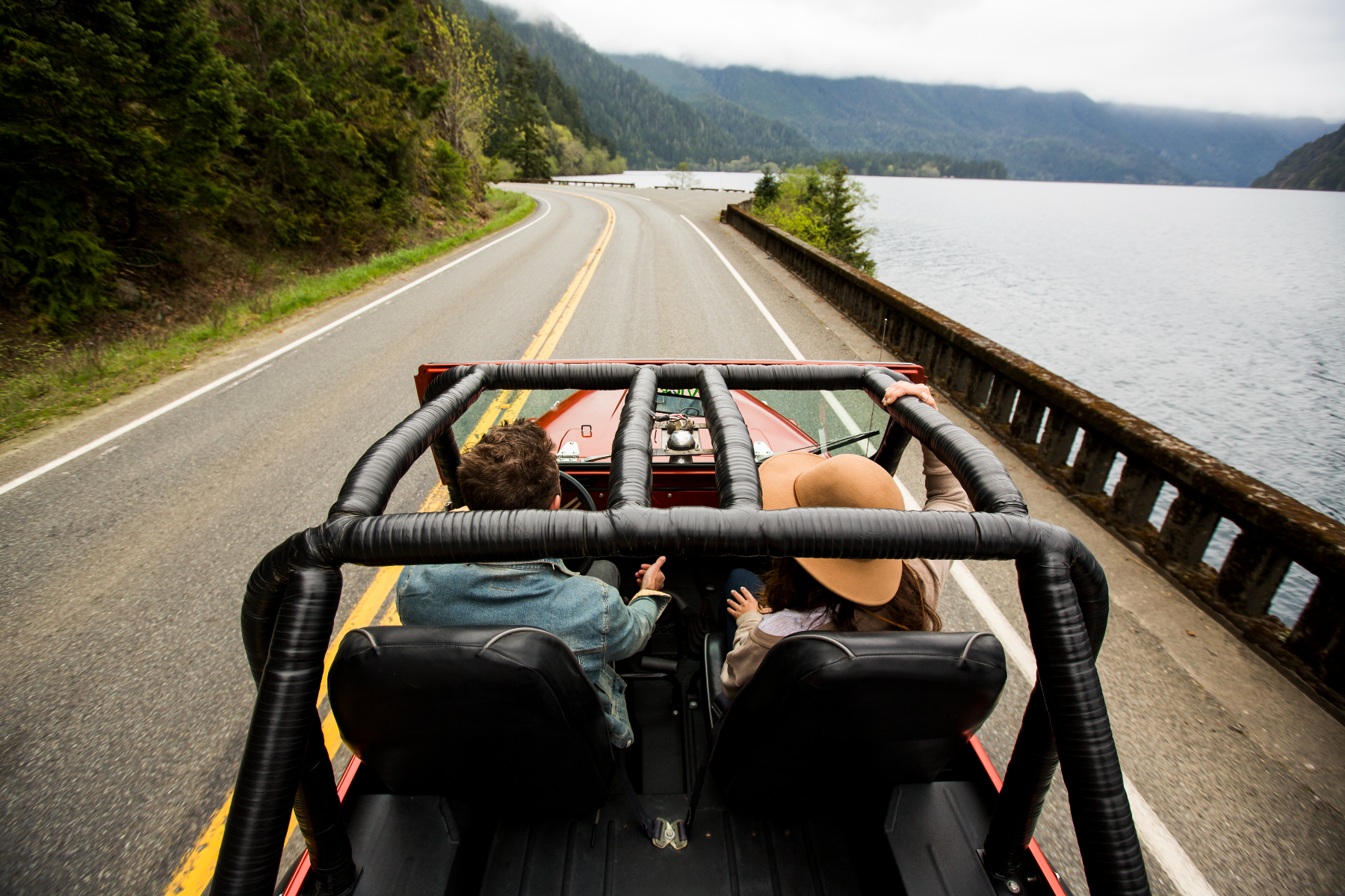 A couple speeding along a two-lane road in their convertible jeep