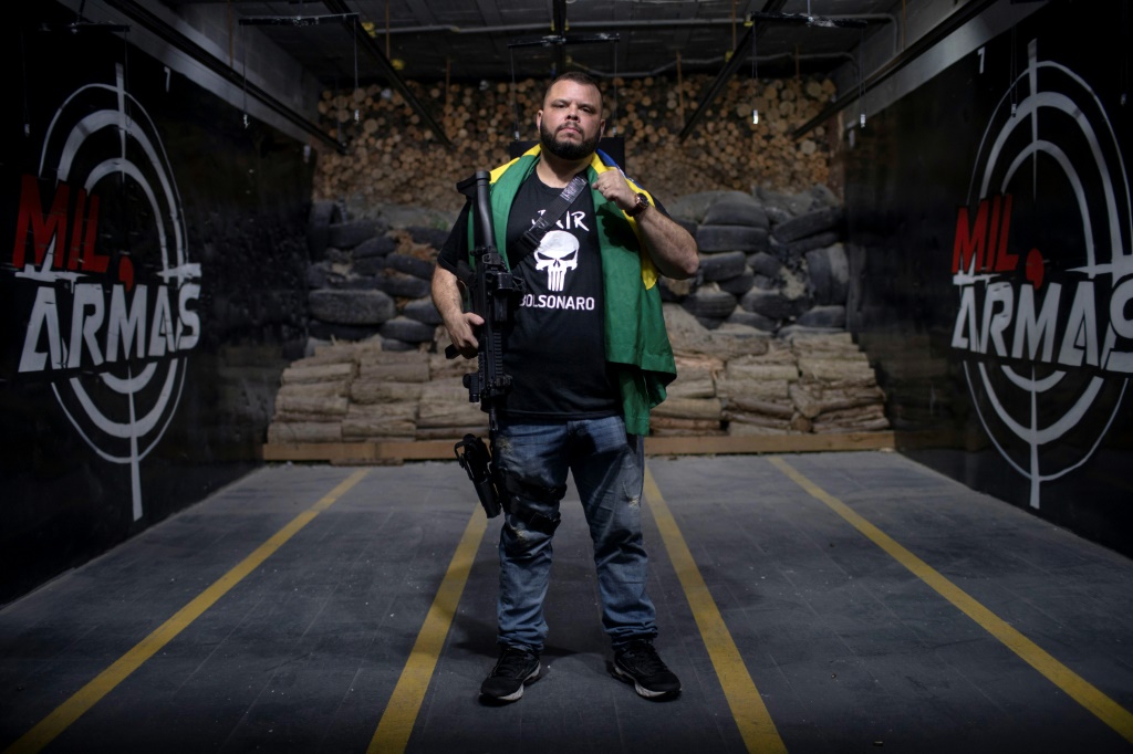 Former Military Police Major Elitusalem Gomes de Freitas, wearing a t-shirt bearing the name of Brazilian President Jair Bolsonaro, poses for a picture carrying his guns and the Brazilian flag, in the city of Nova Iguacu