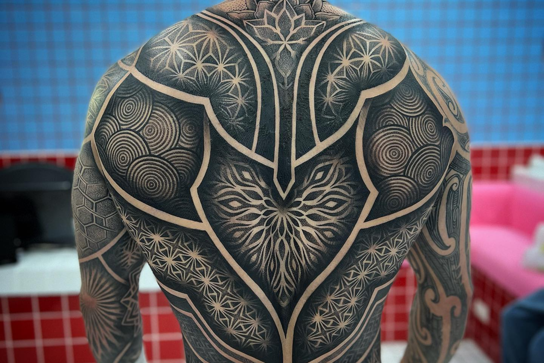 A man has his back covered with a mandala geometric dotwork tattoo