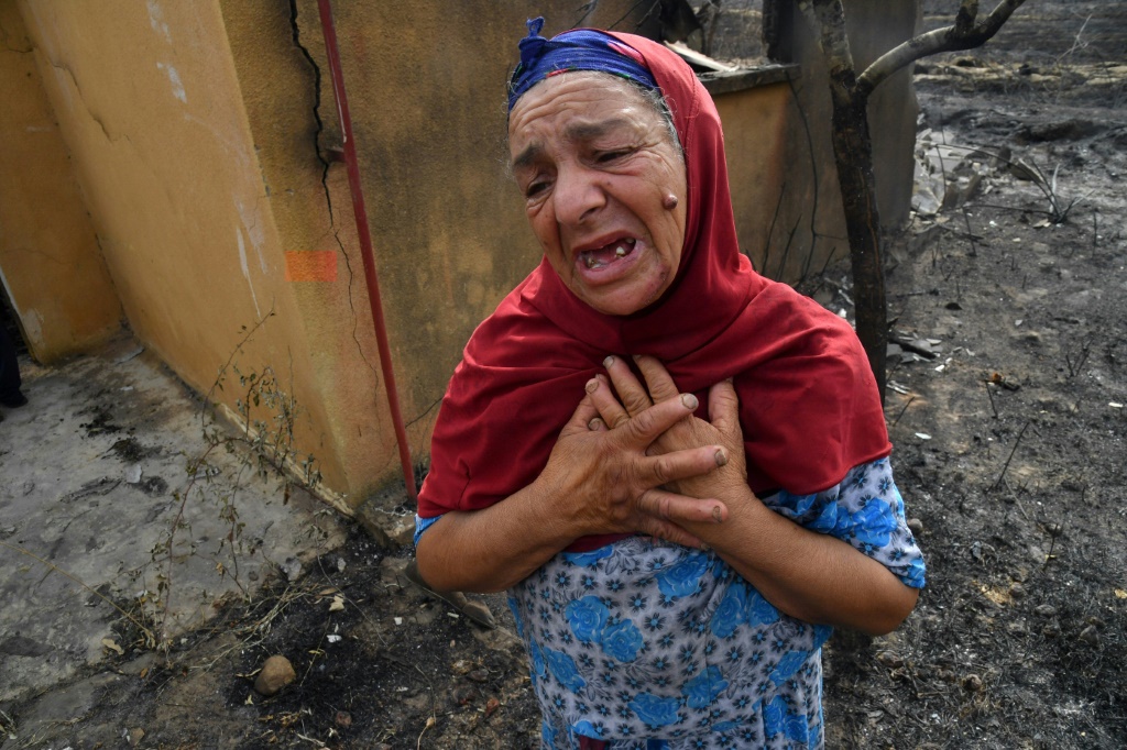 An elderly Algerian woman reacts in front of the ruins of her home, destroyed in a wildfire in the city of El-Kala