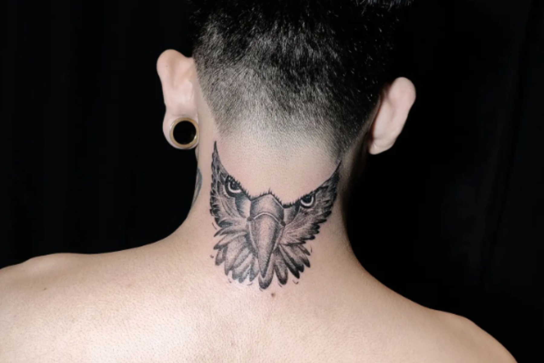 A white man is wearing a half-owl tattoo on the back of his neck