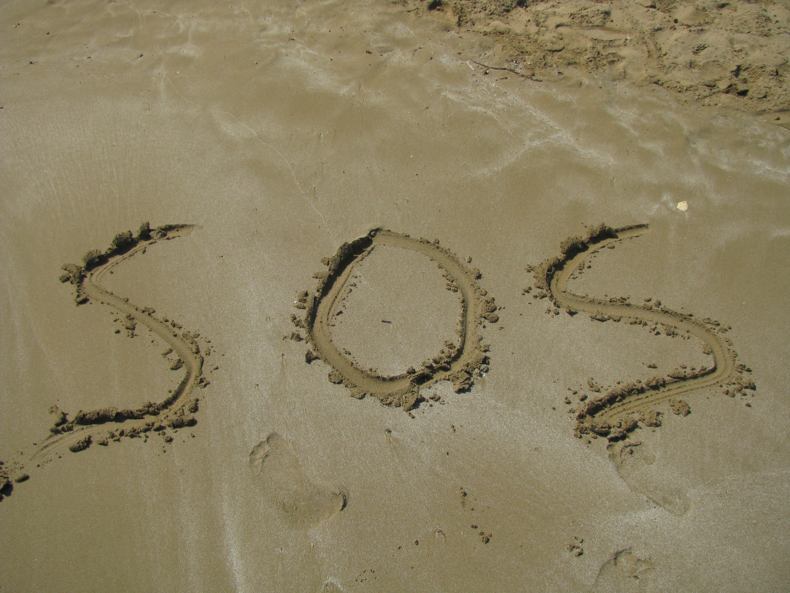 The word 'sos' is written on the sand on the beach.