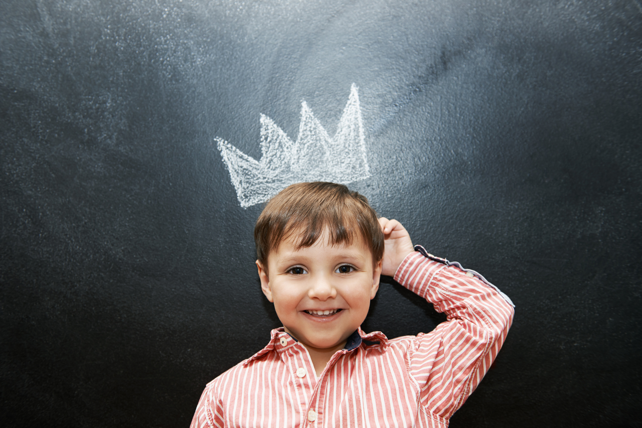 A boy is standing next to a blackboard with a crown drawing.
