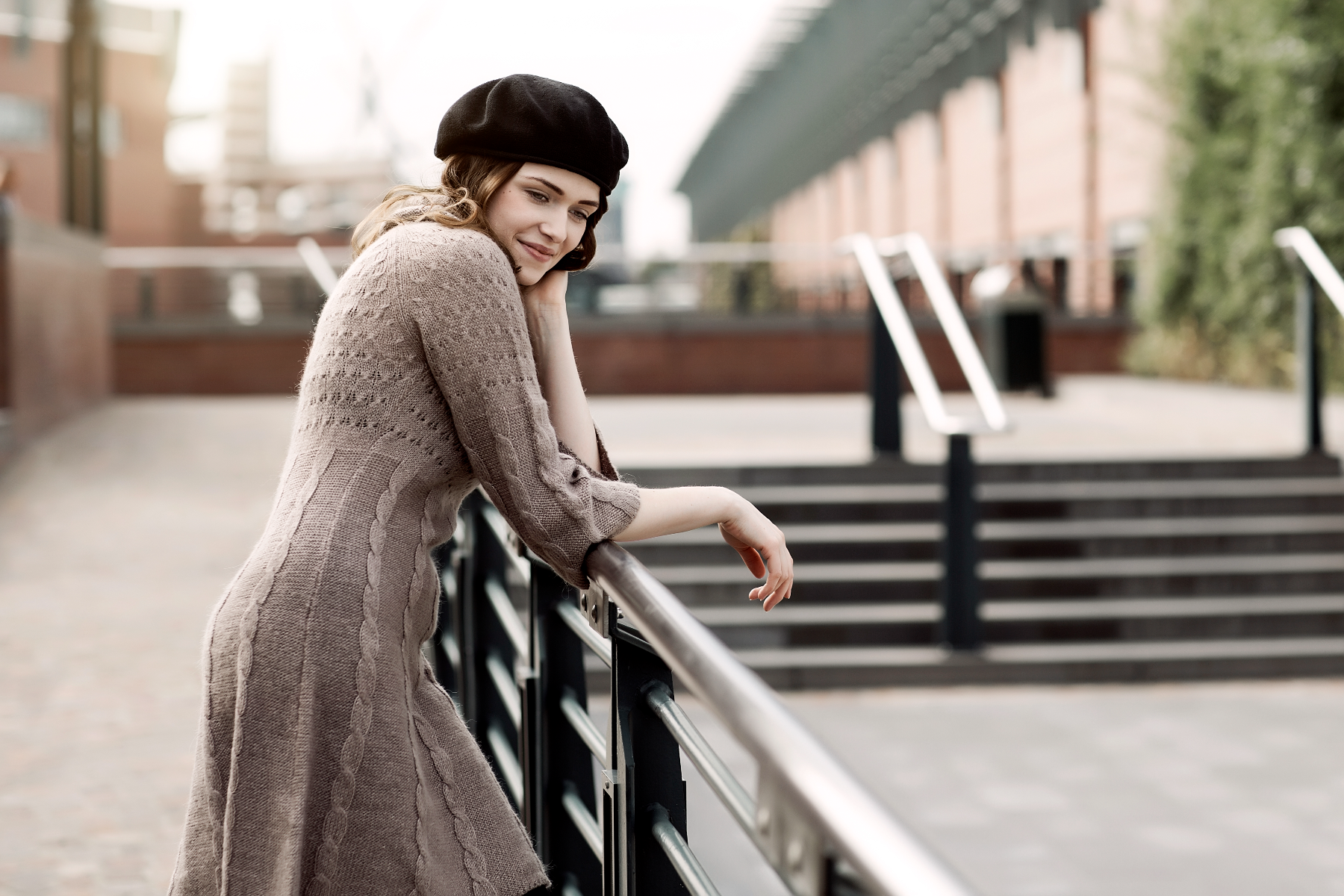 Portrait of a young woman wearing a beret and knitted dress leaning on a railing